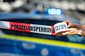 Polizeiabsperrung.jpeg       -  Ein Absperrband wird vor einem Polizeiwagen ausgerollt.