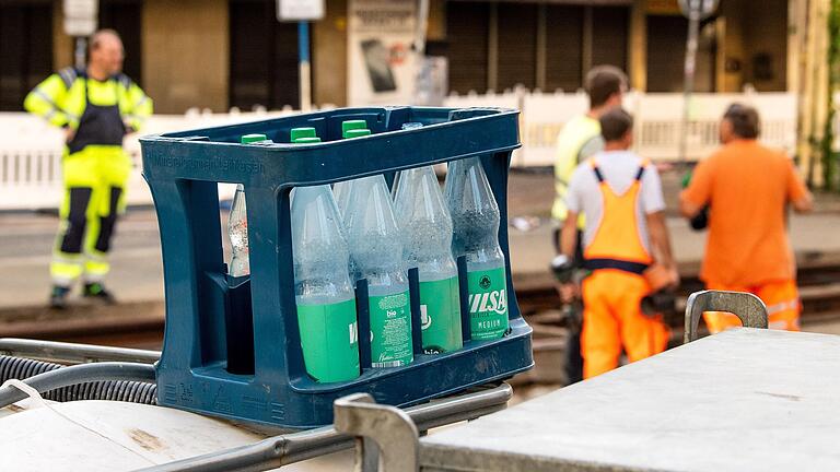 Ein Kasten mit Wasserflaschen steht auf einer Baustelle, auf der Bauarbeiter bei hohen Temperaturen an Straßenbahngleisen arbeiten. Die IG BAU drängt auf Gratis-Wasser und -Sonnencreme an Hitzetagen.&nbsp;