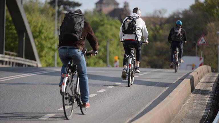 Radfahrer überqueren den durch Striche markierten Radweg über die Grombühlbrücke in Würzburg.