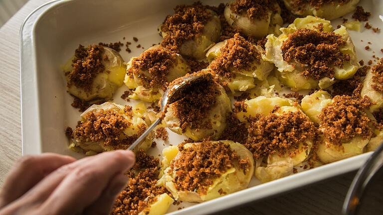 Zubereitung von Smashed Potatoes       -  Sorgt für Knusper-Effekt: Auf die gequetschten Kartoffeln kommt eine Masse aus Pankomehl, geräuchertem Paprikapulver, Rosmarinnadeln, Thymian- und Salbeiblättchen, Salz, Butter und Knoblauch.