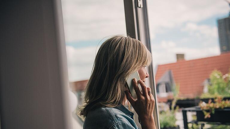 Eine Frau telefoniert am Fenster       -  Fordert bei einem Anruf eine computergenerierte Stimme dazu auf, diesen Kontakt auf Whatsapp hinzuzufügen, blockiert man die Rufnummer am besten gleich.