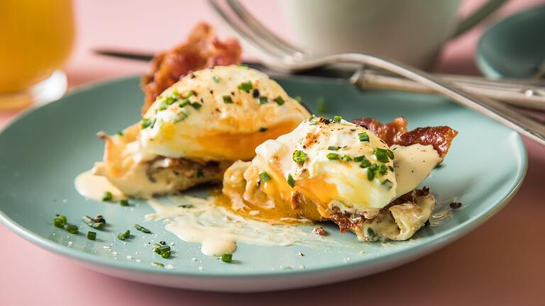 Eggs Benedict am Frühstückstisch       -  Eggs Benedict aus pochierten Eiern, Sauce Hollandaise, Schnittlauch, Paprika-Pulver, Bacon und halbierten englischen Muffins.
