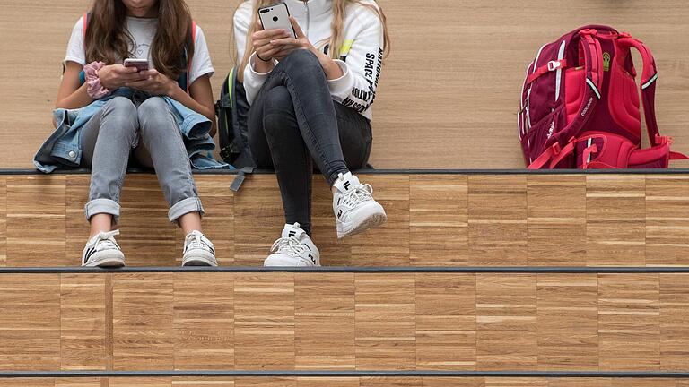 Zwei Schülerinnen mit Smartphone:&nbsp; Das Handyverbot an bayerischen Schulen soll gelockert werden. Am Johann-Schöner-Gymnasium Karlstadt (Lkr. Main-Spessart) dürfen sie schon auch privat genutzt werden – zu bestimmten Zeiten.