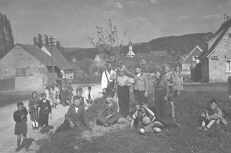 Früher fanden viele Aktivitäten im Freien und innerhalb des Dorfs statt. Am Dorfeingang von Michelau gab es einen Bolzplatz, wo die Kinder Fußball spielten. Im Hintergrund ist der Kirchturm der Balthasar-Neumann-Kirche zu sehen. Früher fanden viele Aktivitäten im Freien und innerhalb des Dorfs statt. Am Dorfeingang von Michelau gab es einen Bolzplatz, wo die Kinder Fußball spielten. Im Hintergrund ist der Kirchturm der Balthasar-Neumann-Kirche zu sehen.