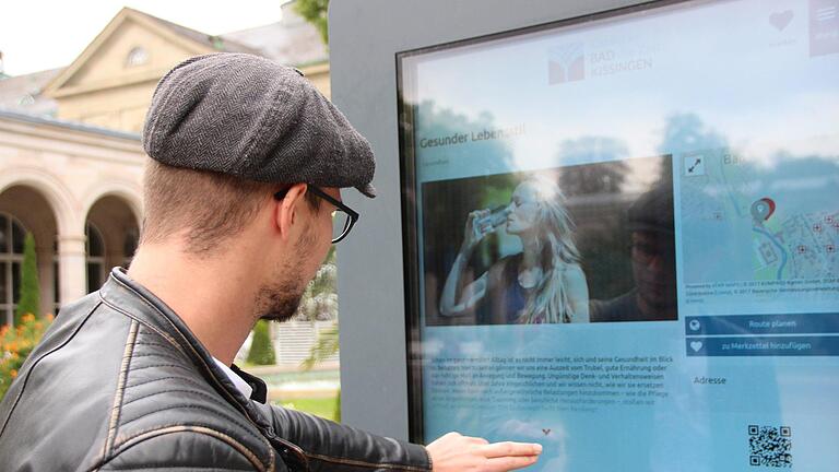 Ein Gast liest an der interaktiven Infostele im Kurgarten. Foto: Benedikt Borst       -  Ein Gast liest an der interaktiven Infostele im Kurgarten. Foto: Benedikt Borst