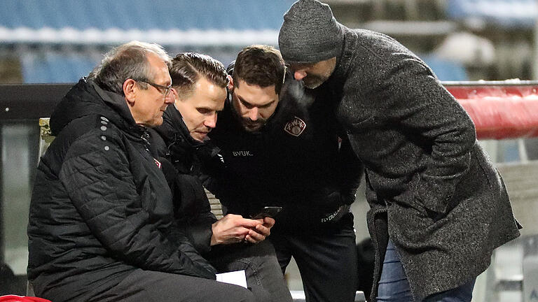 Fassunglos ob eines unberechgten Elfmeterpfiffs (v.li.): Teammanager Norbert Mahler, Vorstand Sport Sebastian Schuppan, Videoanalyst Philipp Eckart und Trainer Bernhard Trares (alle FC Würzburger Kickers) schauen sich den fragwürdigen Elfmeter auf einem Smartphone an.