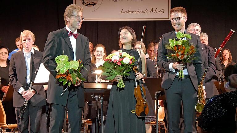 Lebenskraft der Musik verströmte das Windensemble in der Kürnacher Höllberghalle bei einem Benefizkonzert. Beim Abschlussapplaus freuten sich (vorne von links) Dirigent, Initiator und Organisator Wolfgang Heinrich, Solistin Sinn Yang und Moderator Julius Herion.