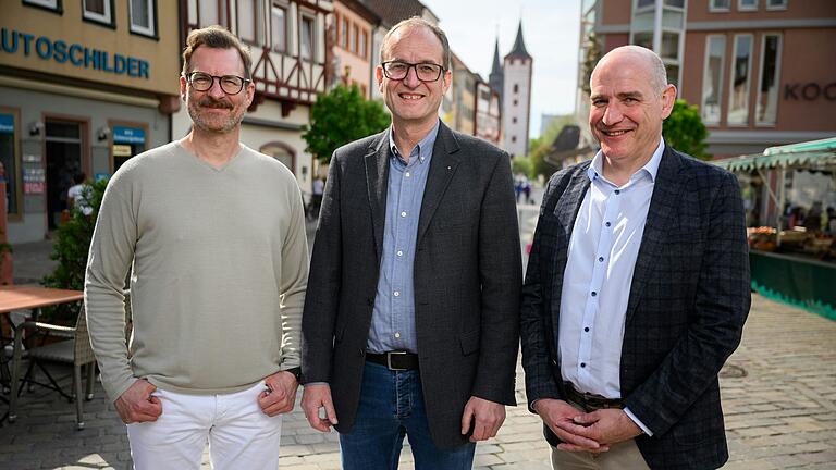 Christoph Weißhaar von der Mohrenapotheke (von links), Karlheinz Schmidt vom Büro-Vollsortimenter Schmidt &amp; Kurtze und Martin Krause vom Modehaus Koch stehen auf dem geschäftigen Marktplatz in Karlstadt. Trotz einiger Leerstände sehen die drei Unternehmer die Zukunft im Karlstadter Zentrum positiv.