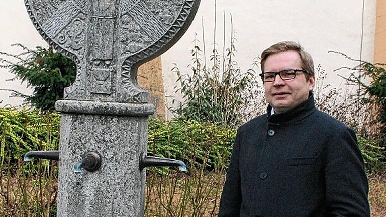 Dettelbachs neuer Stadtpfarrer heißt Uwe Hartmann. Hier steht er neben dem von Pater Raphael Konrad, einem seiner Vorgänger, entworfenen Franziskusbrunnen im Klosterhof.