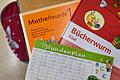 Bücher und ein Stundenplan auf der Schulbank eines Erstklässlers. Foto: Patrick Pleul/Symbolbild       -  Bayerns Grundschüler sollen besser in Deutsch und Mathe werden.