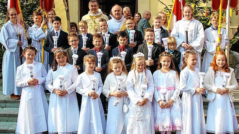 Ein großer Tag für die Kommunionkinder       -  (db)   Wie groß die Pfarreiengemeinschaft Wiesentheid ist, war am vergangenen Wochenende daran zu merken, dass zum zweiten Mal in Stadelschwarzach das Fest der heiligen Kommunion gefeiert wurde, da die Pfarrkirche in Wiesentheid wegen Renovierung noch geschlossen ist. Für 18 Kinder aus der Pfarrei Wiesentheid war deshalb der vergangene Sonntag ihr großer Tag. Die Kommunionfeier in der Stadelschwarzacher St. Bartholomäus-Kirche stand unter dem Motto &bdquo;Sei ein lebendiger Fisch&ldquo;. Der Gottesdienst in der herrlich geschmückten Pfarrkirche in Stadelschwarzach wurde von Pfarrer Peter Göttke und Diakon Karl Leierseder zelebriert. Leierseder war es auch, der in den vergangenen Monaten zusammen mit Gruppenmüttern die Kinder auf diesen besonderen Tag vorbereitete.  Für die musikalische Gestaltung am Festtag sorgten neben dem Organist Andreas Schaar, die Wiesentheider Kirchenband unter der Leitung von Jonas Schug und die Musikkapelle Wiesentheid, die den feierlichen Zug durch die Ortschaft zur Kirche anführte. Die erste heilige Kommunion empfingen: Steven Böttger, Eva Fehlbaum, David Fincher, Christian Giehl, Moritz Grau, Dafin Grunasi, Jannick Hahn, Liam Heining, Mira Hergeth, Anika Hofmann, Olaf Kestler, Amanda Klindt, Julius Kober, Leonie Mühlfried, Melanie Ritz, Nico Schmied, Jonas Stühler, Milena Troglauer. Das Bild zeigt die Kommunionkinder mit Pfarrer Peter Göttke, Diakon Karl Leierseder und den Ministranten (im Hintergrund) am Eingangsportal der Stadelschwarzacher Kirche.