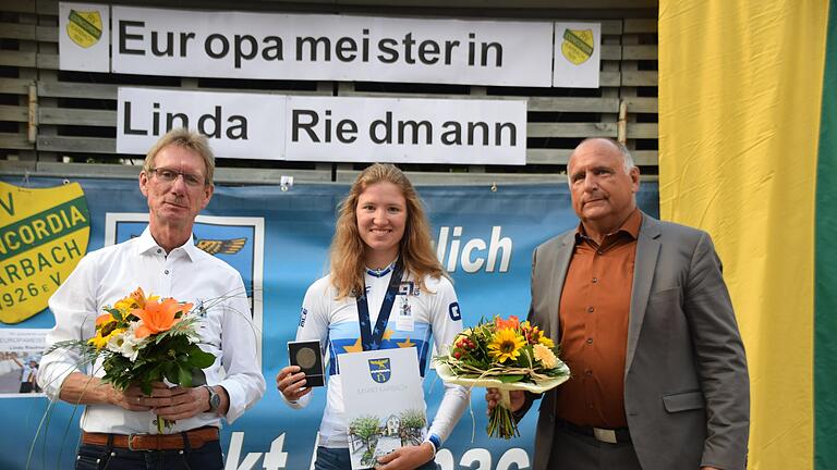 Freudestrahlend präsentiert Linda Riedmann ihre Goldmedaille und die Kommunale Ehrenmedaille der Gemeinde in Bronze. Bürgermeister Bertram Werrlein (rechts) und Berthold Väth (links), der Ehrenvorsitzende des Radfahrvereins Concordia Karbach, freuen sich mit der neuen Europameisterin.