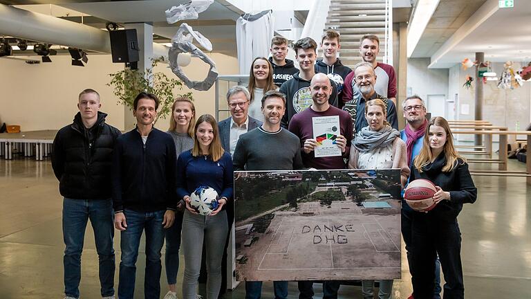 Das Foto zeigt Jürgen Seitz Organisator des Sportprojekts der SportsCharity Mwanza (mit Schild); rechts von ihm: Michael Stolz, Vorsitzender Mwanza e. V.; das Lehrerteam mit OStR Andreas Weiermann (vorne Mitte), OStRin Katharina Schallmaier (vorne, 3. von rechts), OStR Anton Kramer (2. von rechts) und OStR Michael Pietschmann (2. von links) sowie Schulleiter OStD Michael Schmitt (5. von links) und die künftigen „DHG-Sportbotschafter“ in Mwanza.