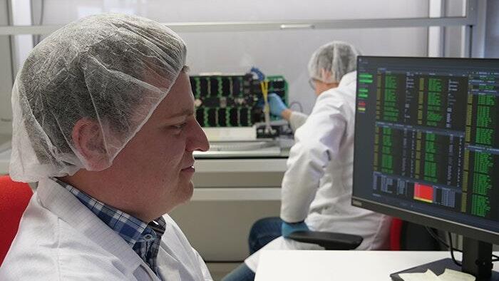 Projektmitarbeiter Andreas Maurer und Projektleiter Dr. Oleksii Balagurin (im Hintergrund) arbeiten im Reinraum am Nanosatelliten SONATE-2. Projektmitarbeiter Andreas Maurer und Projektleiter Dr. Oleksii Balagurin (im Hintergrund) arbeiten im Reinraum am Nanosatelliten SONATE-2.