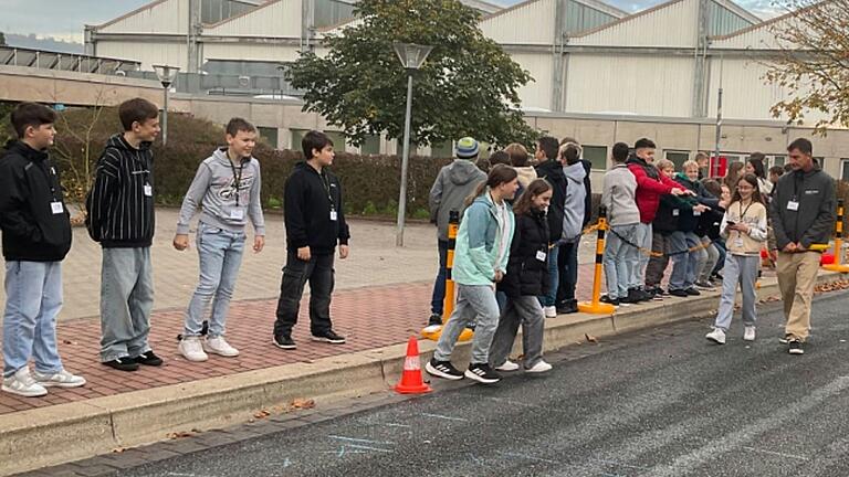 Die Schülerin, die gerade auf der Fahrbahn eine Kurznachricht tippt, bekommt von ihren Klassenkameraden nichts mit, obwohl diese sich lautstark bemerkbar machen.
