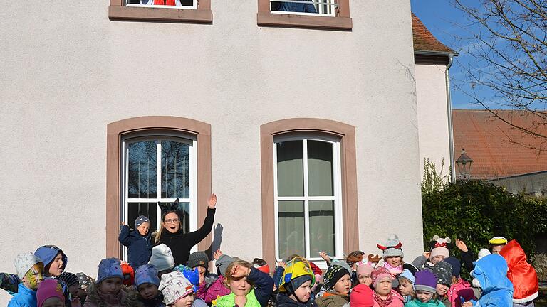 Im Bild das „Heer“ von Kita-Leiterin Daniela Reuß (Bildmitte hinten) vor dem Rathaus. Von oben grüßen die „Burgherrin“ Eva Linsenbreder (links) und ihre „Waffenschwester“ Waltraud Kiesel-Knobloch (rechts) die Kinder. Alle freuen sich über den gelungenen Faschingsspaß.