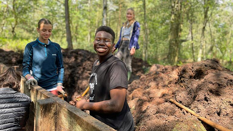 Der südafrikanische Schüler Reha Mukwevo (mitte) von der Southern Cross School aus Hoedspruit ist mit vollem Eifer beim Bau des Stauwehres im Schwarzen Moor dabei. Auch Clara Fatt (links) vom Martin-Pollich-Gymnasium packt kräftig mit an.&nbsp;