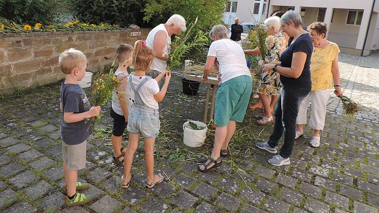 Mit großem Interesse verfolgten die Kinder das Binden von Kräutersträußchen beim Frauenbund Hofheim. Im Hintergrund&nbsp;Pfarrvikar Ninh.