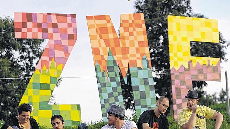 Auf der Wiese entspannt der Musik lauschen: Zuhörerer sitzen am Mittwoch bei der Eröffnung zum 30. Zeltmusikfestival (ZMF) in Freiburg im Rasen vor dem Logo des ZMF. Bis zum 22.Juli treten zahlreiche Musiker in verschiedenen Zelten auf.