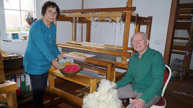 Silvia und Wolfgang Kisperth mit selbst gesponnener Wolle zwischen ihren Webstühlen, vorne frisch gewaschene Schafwolle im Korb zum Spinnen von Wollfäden.