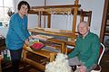 Silvia und Wolfgang Kisperth mit selbst gesponnener Wolle zwischen ihren Webstühlen, vorne frisch gewaschene Schafwolle im Korb zum Spinnen von Wollfäden.
