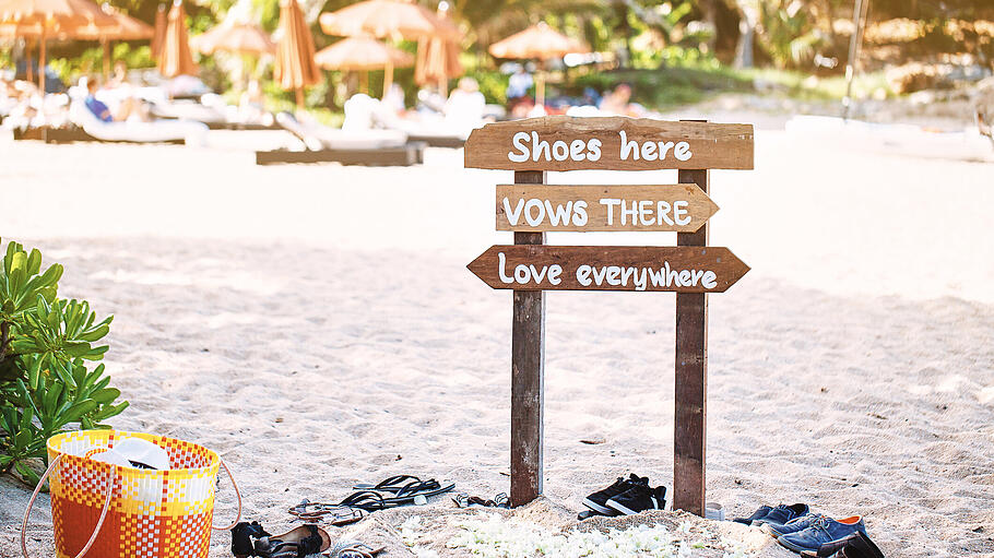 Wooden banner on the beach with text 'Shoes here, Vows there, Love everywhere' at the wedding venue       -  Schuhe verboten: bei einer Strandhochzeit ist lockere Atmosphäre vorausgesetzt.