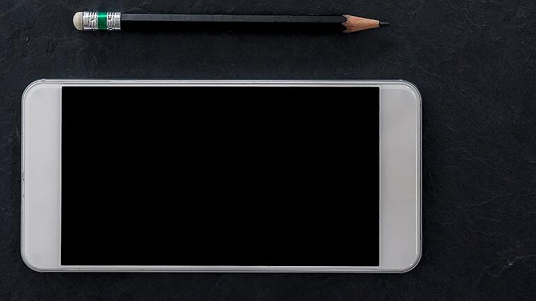 cell phone and black pencil on black stone background. flat lay style       -  _