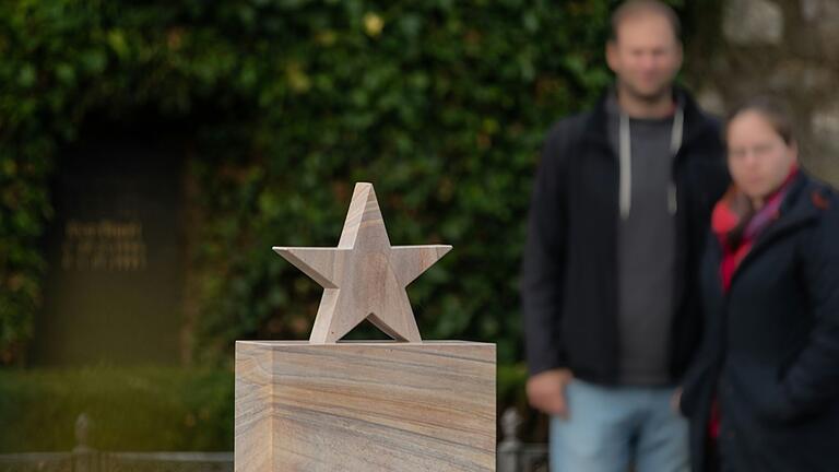 Michael und Maria stehen vor der neuen Stele für Sternenkinder auf dem Friedhof in Volkach. Die Eltern haben selbst ein Kind verloren und nun einen Ort zum Trauern.