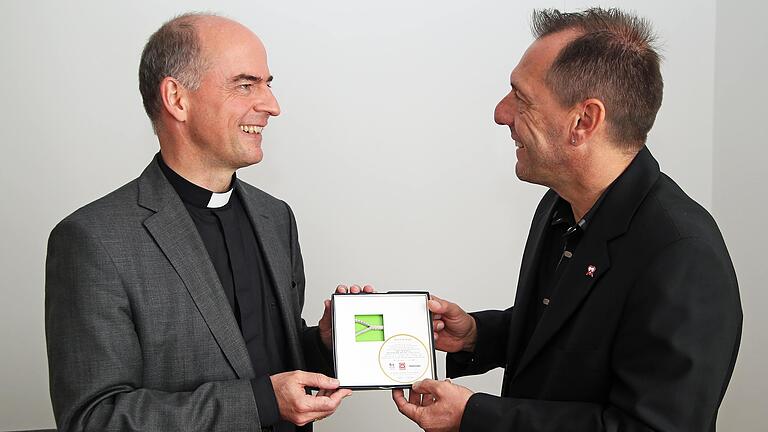 Bischof Dr. Franz Jung (links) erhält von DAHW-Geschäftsführer Burkard Kömm ein Stück Original-Tornetz vom Spiel Deutschland gegen Brasilien bei der Fußballweltmeisterschaft 2014.