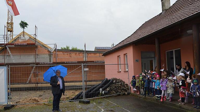 Richtfest an neuer Kindertagesstätte in Birkenfeld       -  (sec)   &bdquo;Im Kindergarten, im Kindergarten, da fangen alle mal als kleine Leute an...&ldquo;, sangen die Kinder aus dem Birkenfelder Kindergarten beim Richtfest für die neue Kindertagesstätte. Allerdings machte das schlechte Wetter Bürgermeister Achim Müller einen Strich durch die Rechnung. Kurzerhand verlegte er das Richtfest an die Rückseite des Neubaus, an den  Eingangsbereich des Pfarrheims, wo die Kindergartenkinder ein trockenes Plätzchen fanden. Gerade mal 141 Tage nach dem Spatenstich im März konnte das Richtfest  gefeiert werden. Müller dankte allen am Bau Beteiligten, vor allen den fleißigen Handwerkern. Auch die gute Kooperation mit dem Architekturbüro Georg Redelbach hob Müller hervor. Das neue Gebäude, das mit knapp zwei Millionen Euro veranschlagt ist, bietet im nächsten Jahr weitere 33 Kleinkindplätze in Birkenfeld. Aus luftiger Höhe trug Zimmerer Olaf Palmer den gereimten Richtspruch vor. Traditionell zerschmetterte der Handwerker sein Glas schließlich am Mauerwerk des Neubaus und wünschte Glück und Segen. Anschließend bekamen die Kindergartenkinder Süßigkeiten und der Bürgermeister lud die Anwesenden zu einem Essen ins Pfarrheim ein.