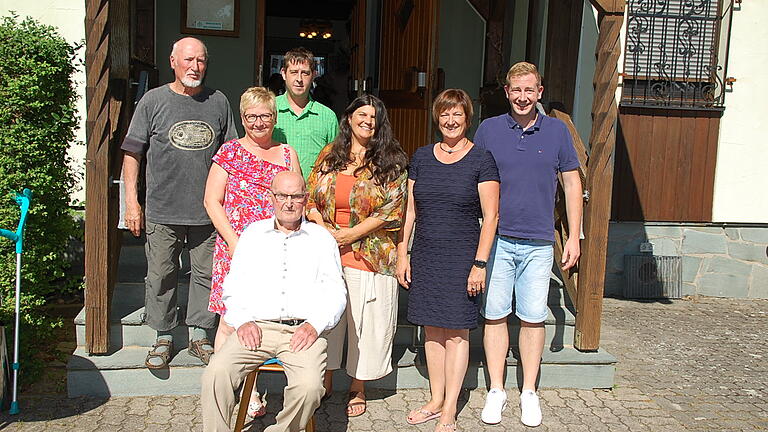 Der Jubilar sitzend im Kreis der Vereinsvertreter vor dem Wanderheim der Heimat- und Wanderfreunde: (von links) Richard Rüppel (Gesangverein), Inge Deffner (DJK Oberndorf), Tobias Väth (Heimat- und Wanderfreunde), Karin König (OCV), Bürgermeisterin Agnes Engelhardt und Sebastian Weidner (Feuerwehr).