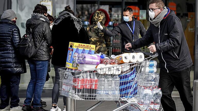 Coronavirus - Italien       -  Menschen mit Atemschutzmasken stehen vor einem Supermarkt in der Lombardei Schlange und versorgen sich mit Lebensmitteln. Nach der Ausbreitung des Coronavirus sind Teile des öffentlichen Lebens in Norditalien zum Erliegen gekommen.