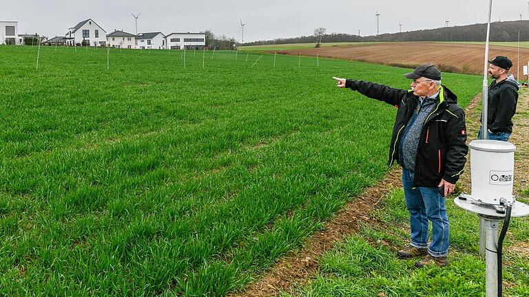 Nur die hellen Stangen im Acker und Messgeräte am Rand (rechts) deuten auf den Versuch hin: Agraringenieur Karl Wieland zeigt auf das Feld am Rand von Güntersleben (Lkr. Würzburg), wo TransnetBW den SuedLink-Betrieb simuliert.