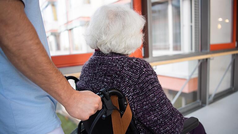 Ein Pfleger schiebt in einem Heim eine Seniorin im Rollstuhl. Weil immer mehr Beschäftigte coronabedingt ausfallen, steht die Versorgung von Heimbewohnern teilweise auf der Kippe (Symbolbild).