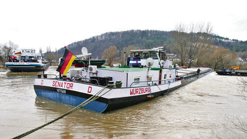 Das Frachtschiff &bdquo;Senator&ldquo; liegt an beiden Ufern verkeilt auf dem Main vor dem Hafen des Zementwerks Schwenk. Die Strömung drückt mächtig gegen das 100 Meter lange Schiff mit 2,50 Metern Tiefgang. Links im Bild die &bdquo;Bavaria 80&ldquo;, die zunächst alleine versuchte, mit ihren 2000 PS das Schiff freizubekommen.