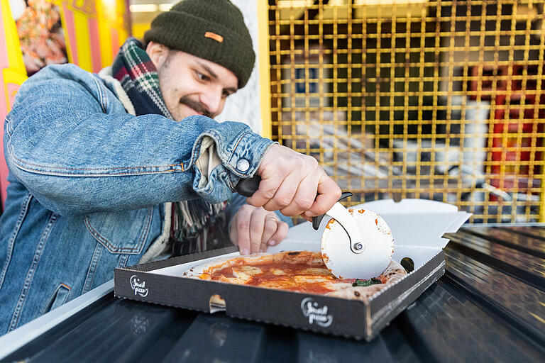 Vittorio Simonetti, Bruder von Flavio Simonetti und ebenfalls Betreiber des Pizza Automaten in Rimpar, schneidet eine frisch bestellte Automatenpizza.