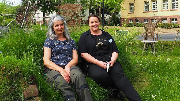 Gärtnerin Dorothee Fuchs und Psychotherapeutin Tina Gast sitzen auf der grünen Wiesencouch des Schmetterlingsgartens am Bezirkskrankenhaus Lohr. Gemeinsam machen sie die Gartentherapie möglich.