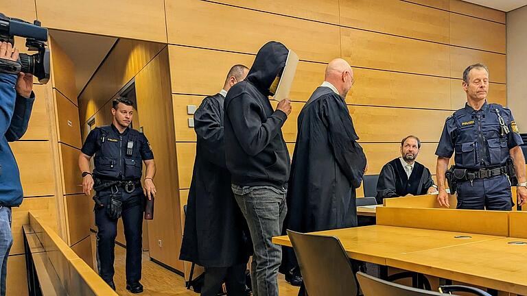 Der 22-jährige Angeklagte am ersten Prozesstag mit Fußfesseln und verdecktem Gesicht auf dem Weg zur Anklagebank des Würzburger Landgerichts. Der 22-jährige Angeklagte am ersten Prozesstag mit Fußfesseln und verdecktem Gesicht auf dem Weg zur Anklagebank des Würzburger Landgerichts.