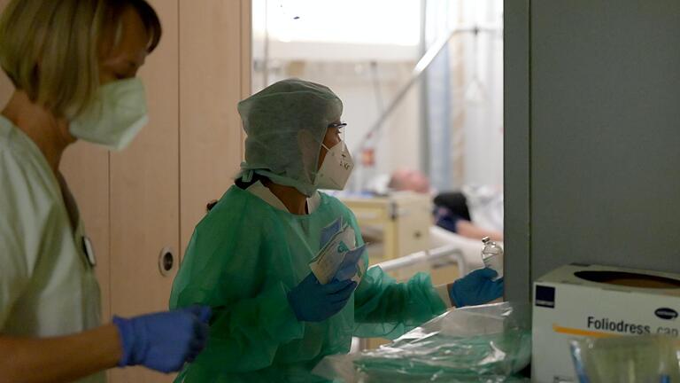 Angelica Kritzner betritt ein Krankenzimmer, draußen dokumentiert eine Kollegin Sauerstoffsättigung und Blutdruck. Angelica Kritzner betritt ein Krankenzimmer, draußen dokumentiert eine Kollegin Sauerstoffsättigung und Blutdruck.