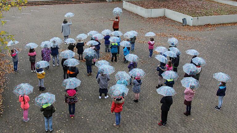 Schülerinnen und Schüler mit den gespendeten Regenschirmen im Pausenhof. Hinten im Bild die aufgezeichneten Abstandslinien vor dem Schuleingang. Schülerinnen und Schüler mit den gespendeten Regenschirmen im Pausenhof. Hinten im Bild die aufgezeichneten Abstandslinien vor dem Schuleingang.