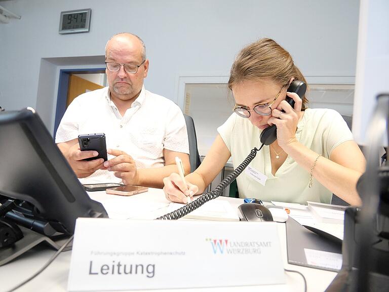 Nina Opfermann, Leiterin der Führungsgruppe Katastrophenschutz am Landratsamt Würzburg, nimmt den wichtigen Anruf des Kreisbrandrats Michael Reitzenstein entgegen, der das Unfallszenario in Veitshöchheim beschreibt. Paul Justice, Führungsassistenz, koordiniert bereits die allerersten Schritte. Nina Opfermann, Leiterin der Führungsgruppe Katastrophenschutz am Landratsamt Würzburg, nimmt den wichtigen Anruf des Kreisbrandrats Michael Reitzenstein entgegen, der das Unfallszenario in Veitshöchheim beschreibt. Paul Justice, Führungsassistenz, koordiniert bereits die allerersten Schritte.