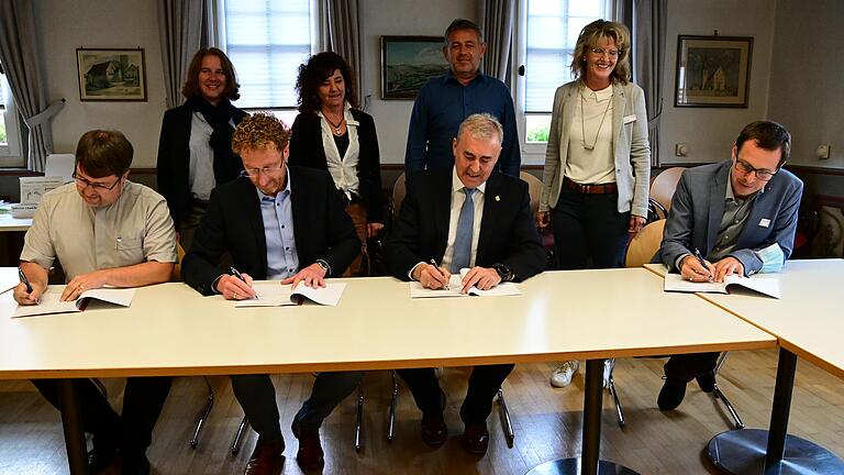 Mit der Unterschrift im Grünsfelder Rathaus von Pfarrer Oliver Störr, Bürgermeister Marcus Wessels, Bürgermeister Joachim Markert und Vorstandsvorsitzender Caritas Matthias Fenger (von links) ist das erste interkommunale Familienzentrum im Main-Tauber-Kreis perfekt. Im Hintergrund (von links): Kindergartenleiterin Katja Baumann, Familienzentrumsleiterin Cornelia Renk, Hauptamtsleiter Jürgen Umminger und&nbsp;Beate Maier, Bereichsleiterin Beratung bei der Caritas .