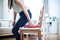 Eine Frau setzt sich auf ein Donutkissen       -  Richtig sitzen: Ein ergonomischer Stuhl oder ein Donutkissen entlasten das Steißbein bei langem Sitzen.