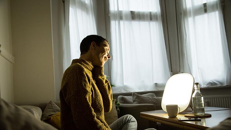Frau sitzt vor einer Tageslichtlampe - Lichttherapie für die Laune - eine Möglichkeit für alle, die tagsüber nicht viel draußen sein können. Frau sitzt vor einer Tageslichtlampe - Lichttherapie für die Laune - eine Möglichkeit für alle, die tagsüber nicht viel draußen sein können.