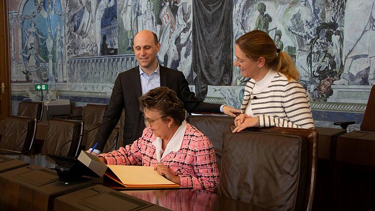 Emmanuelle Chiffre trägt den Namen ihrer Schule „Lycée S. Liégard“ in das Goldene Buch der Stadt Würzburg für Kinder ein. Bürgermeisterin und Schulreferentin Judith Roth-Jörg&nbsp; und Kulturreferent Benedikt Stegmayer beobachten diese Eintragung.