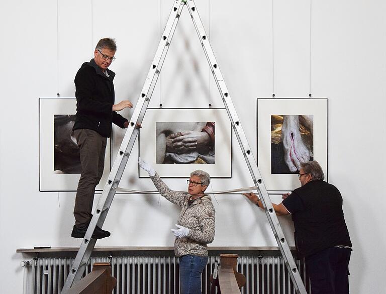 Fotografien von Ralf Luge ergänzen die Ausstellung der Karfreitagsprozessionsfiguren in der Lohrer Klosterkirche. Auf unserem Foto sind Luge, Petra Stegerwald und Joachim Salzmann (von links) beim Aufhängen der Bilder zu sehen.