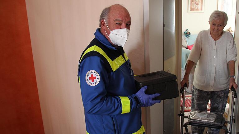 Reiner Schuler fährt beim Roten Kreuz eine Tour des Menüservices. Ingeborg Berz legt er das Essen auf den Rollator, damit sie es bequem in ihre Wohnung tragen kann. Mehr Kontakt ist coronabedingt nicht möglich.&nbsp;