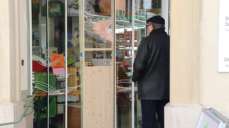 Vor einer Apotheke am Kitzinger Marktplatz wartet ein Mann auf Medikamente. Zum Schutz des Personals ist am Eingang eine Durchreiche eingerichtet.