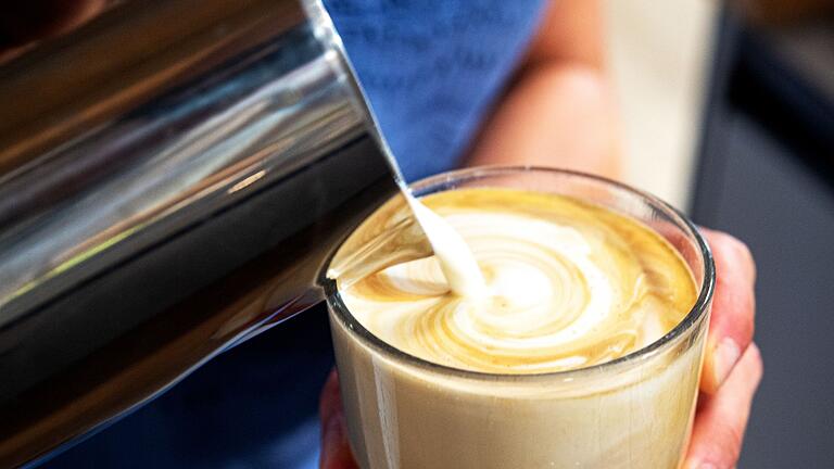 Milchschaum wird aus einer Kanne in ein Glas geschüttet.       -  Schon die Milch im Cappuccino kann zum Problem für Menschen mit einer Laktoseintoleranz werden.