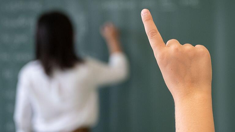 Lehrerin und Schüler.jpeg - Ein Schüler meldet sich, während die Lehrerin an die Tafel schreibt. Lehrerin und Schüler.jpeg - Ein Schüler meldet sich, während die Lehrerin an die Tafel schreibt.